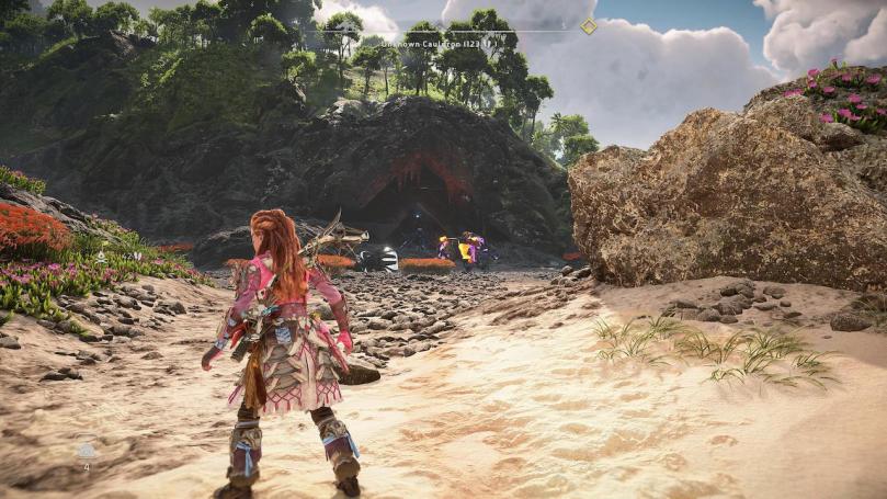 Aloy looking towards the entry of Cauldron THETA in a beach environment with an Apex Fireclaw guarding the way.