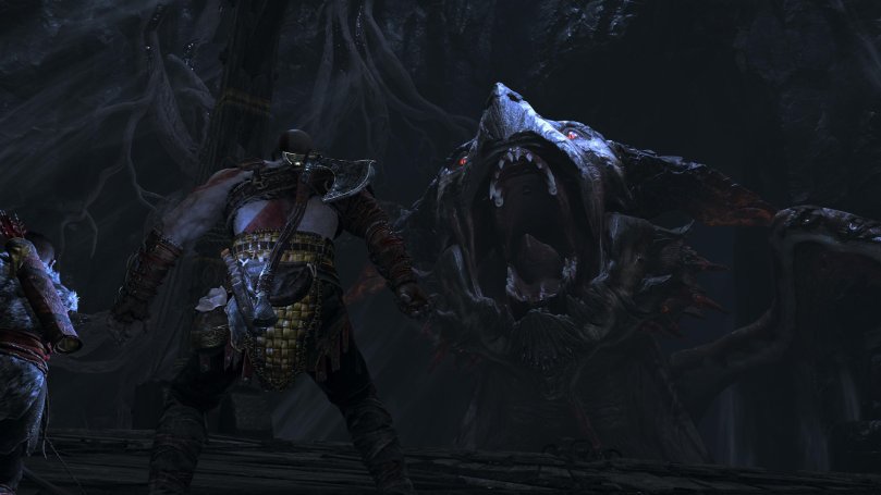 Kratos and Atreus stare into the wide open maw of an angry dragon while riding an ancient elevator to the top of the mine inside a mountain.