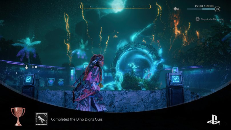 Aloy standing in the middle of fireworks after solving the Dino Digits Quiz. It is a dark and cloudy night and the structures are illuminated in a blue and purple color.