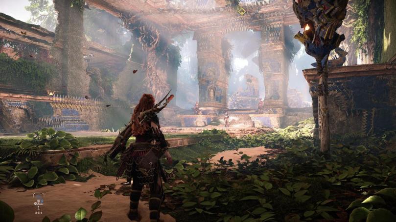 Aloy stands in the overgrown main area of Chief Hekarros throne room that once was a museum. Sunrays are shining through the holes in the walls and the ceiling.